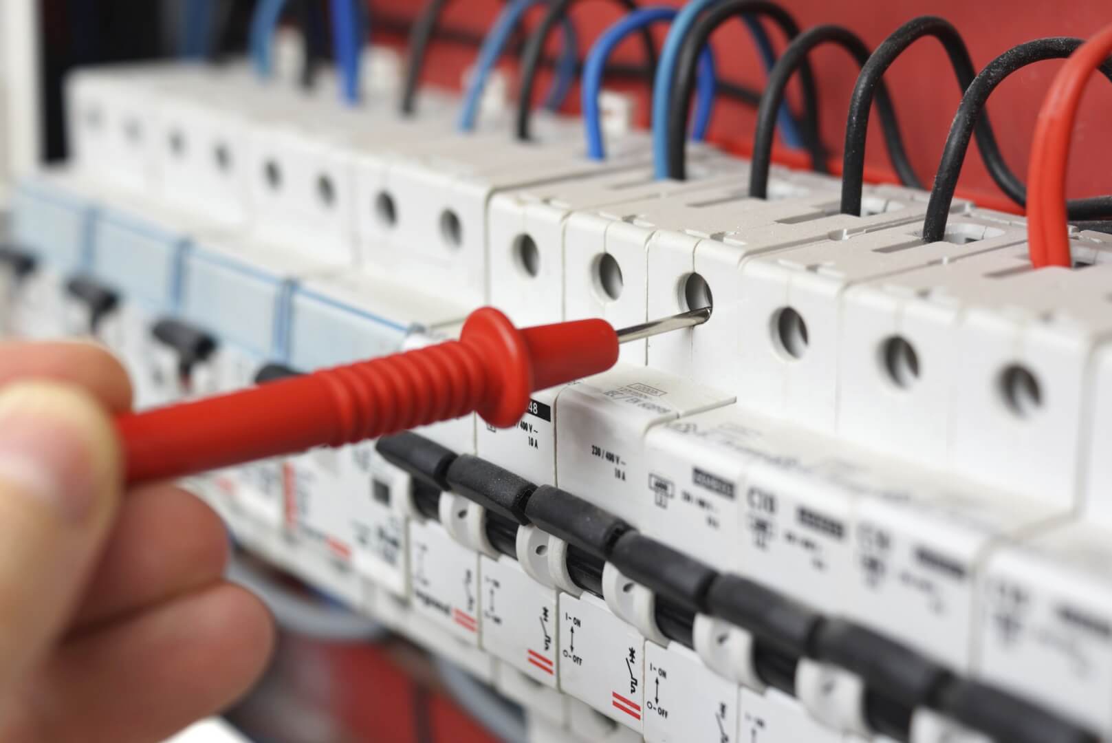 Hand of an electrician with multimeter probe at an electrical sw